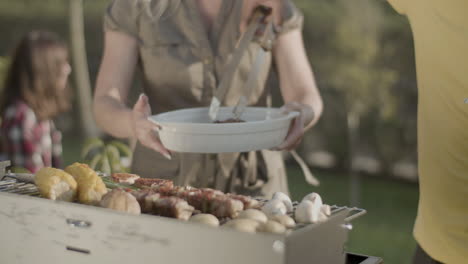 man at barbecue grill putting pork ribs on dish of his wife