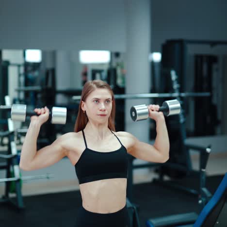 a young woman holds in her hands iron dumbbells and raises it on the background of sports equipment. pumping the biceps in the gym.