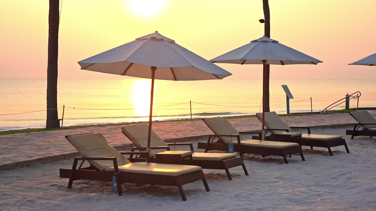 Lounge fronte mare sulla spiaggia con una fila di lettini sotto gli ombrelloni al tramonto dorato sul mare