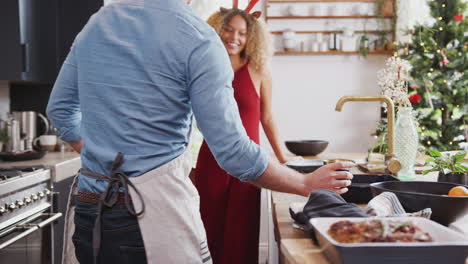 pareja con vestidos de lujo, cuernos y sombrero de papel en casa cocinando una cena vegetariana el día de navidad
