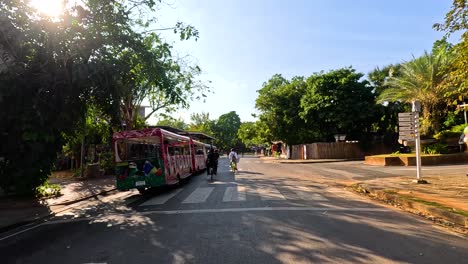 street view of a sunny day in thailand with people biking and a decorated streetcar