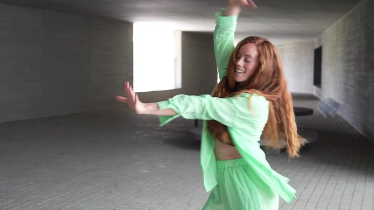 Woman in green outfit happily dancing in modern hallway expressing freedom and happiness