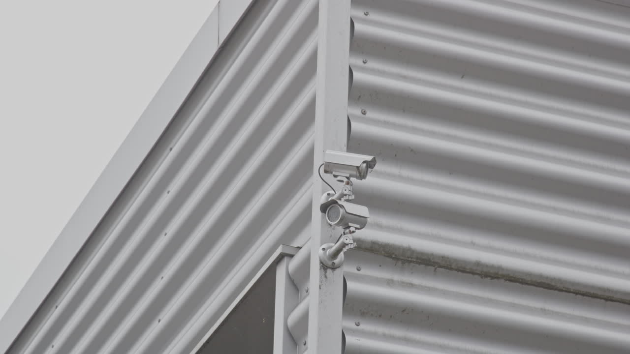 Tilt up to security cameras on the corner of a metal plated warehouse