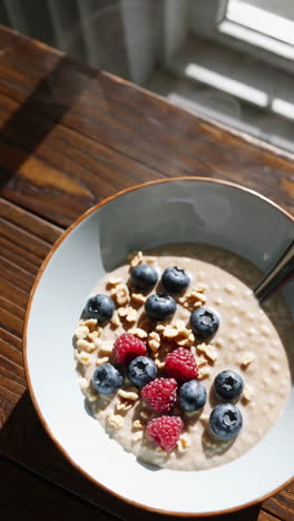 eating a healthy breakfast bowl with oatmeal, blueberries, raspberries, and granola