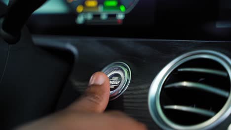 man's thumb pressing the button start stop engine in a car