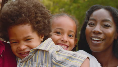 Portrait-Of-Loving-Mixed-Race-Family-Leaning-On-Walk-In-Summer-Countryside