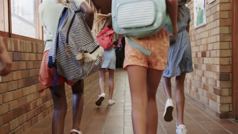 rear view of happy diverse schoolgirls with school bags running in corridor at elementary school