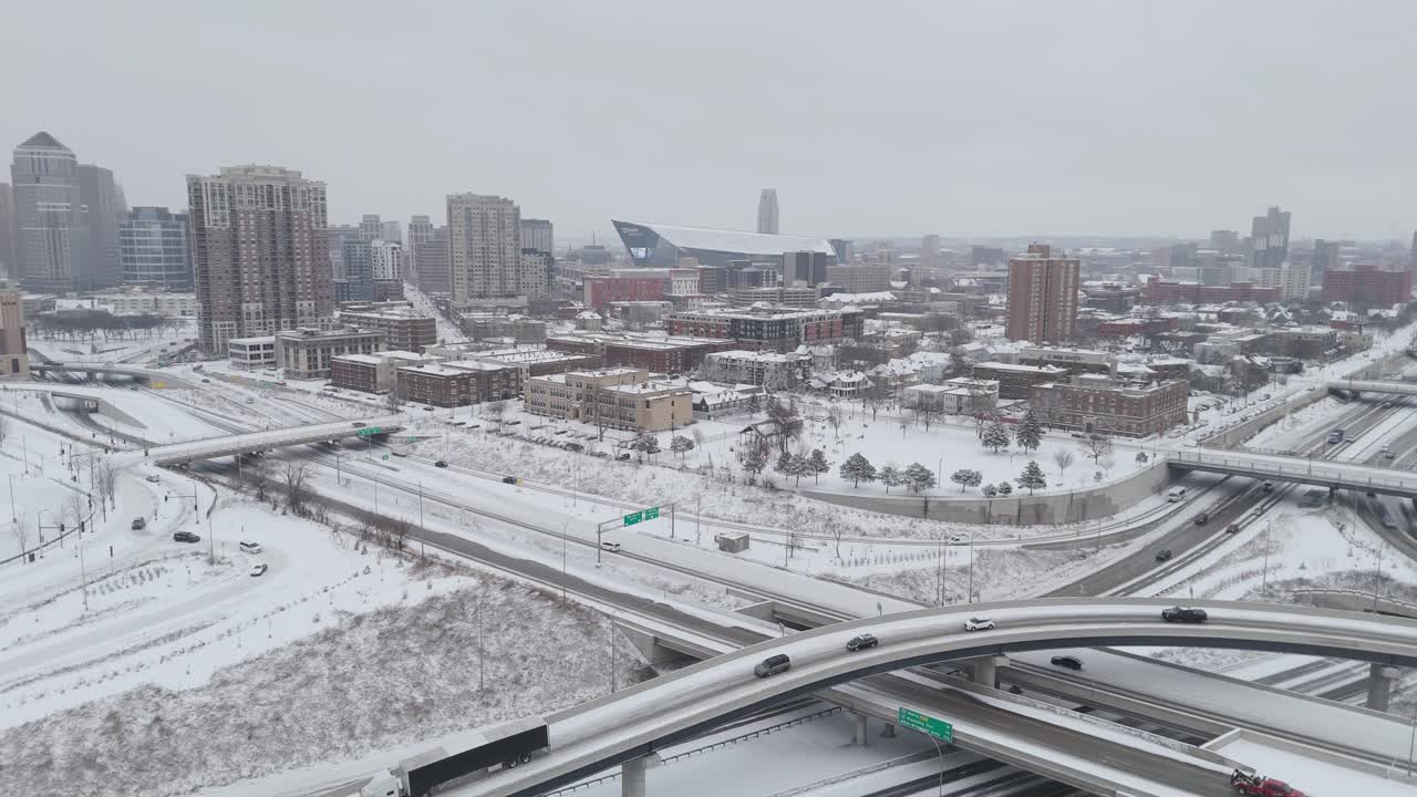 Aerial view of snowy Minneapolis, featuring highways, modern buildings, and the US Bank Stadium under an overcast winter sky.