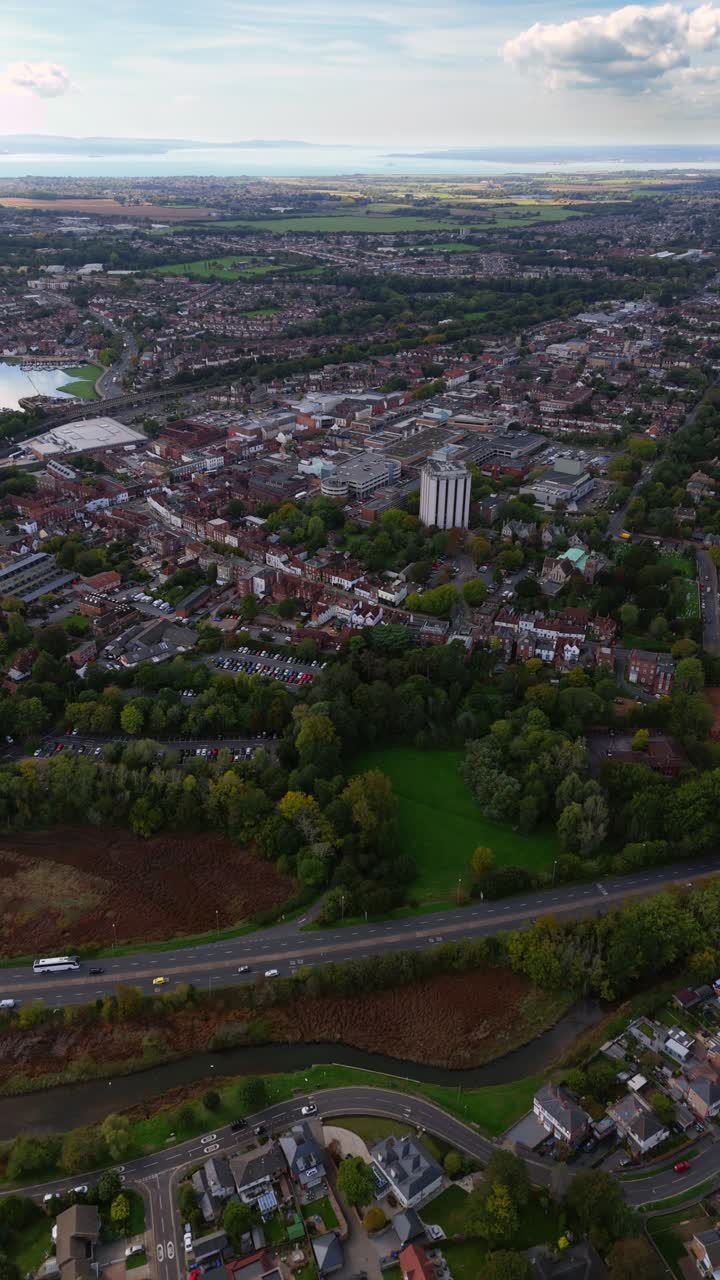 High-angle aerial drone pans left over Fareham town centre, capturing cars, roads, and autumn trees glowing warmly in golden sunset light across the scenic English countryside landscape