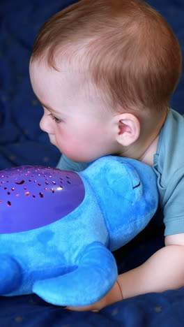 caucasian baby boy lies on his belly with a soft toy in front of him. calm kid looks at toy and then rises eyes to the camera. vertical video