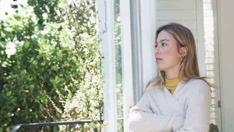 Portrait-of-thoughtful-biracial-woman-looking-through-window-at-home,-slow-motion,-copy-space