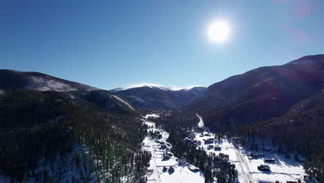 Drone-shot-of-homes-in-a-valley-amongst-mountains-and-dense-forest