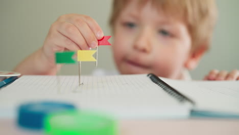 toddler boy replaces pin with small red tag on notebook