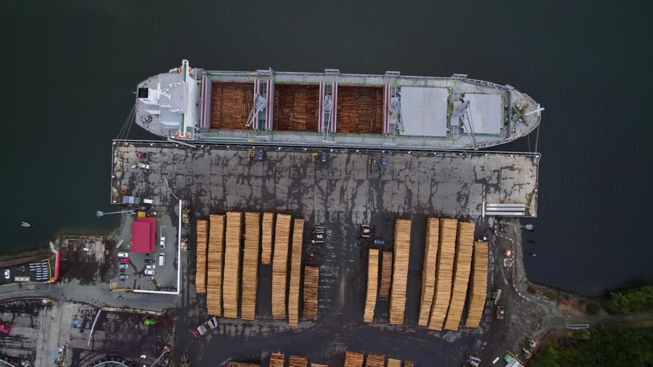 Birds eye drone shot rising above a lumber ship at a timber yard in New Zealand