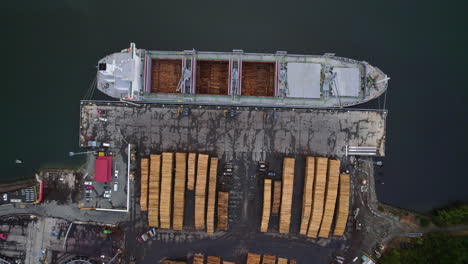 birds eye drone shot rising above a lumber ship at a timber yard in new zealand