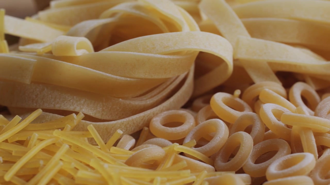 Primo piano di varie forme di pasta secca, incluse tagliatelle, fusilli e anellini