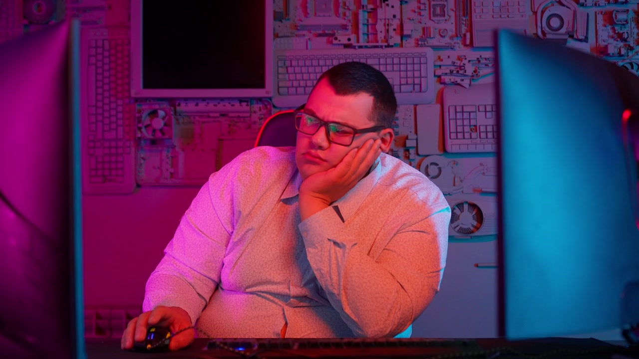 Tired Man with Glasses at Computer Desk in Neon Lit Room