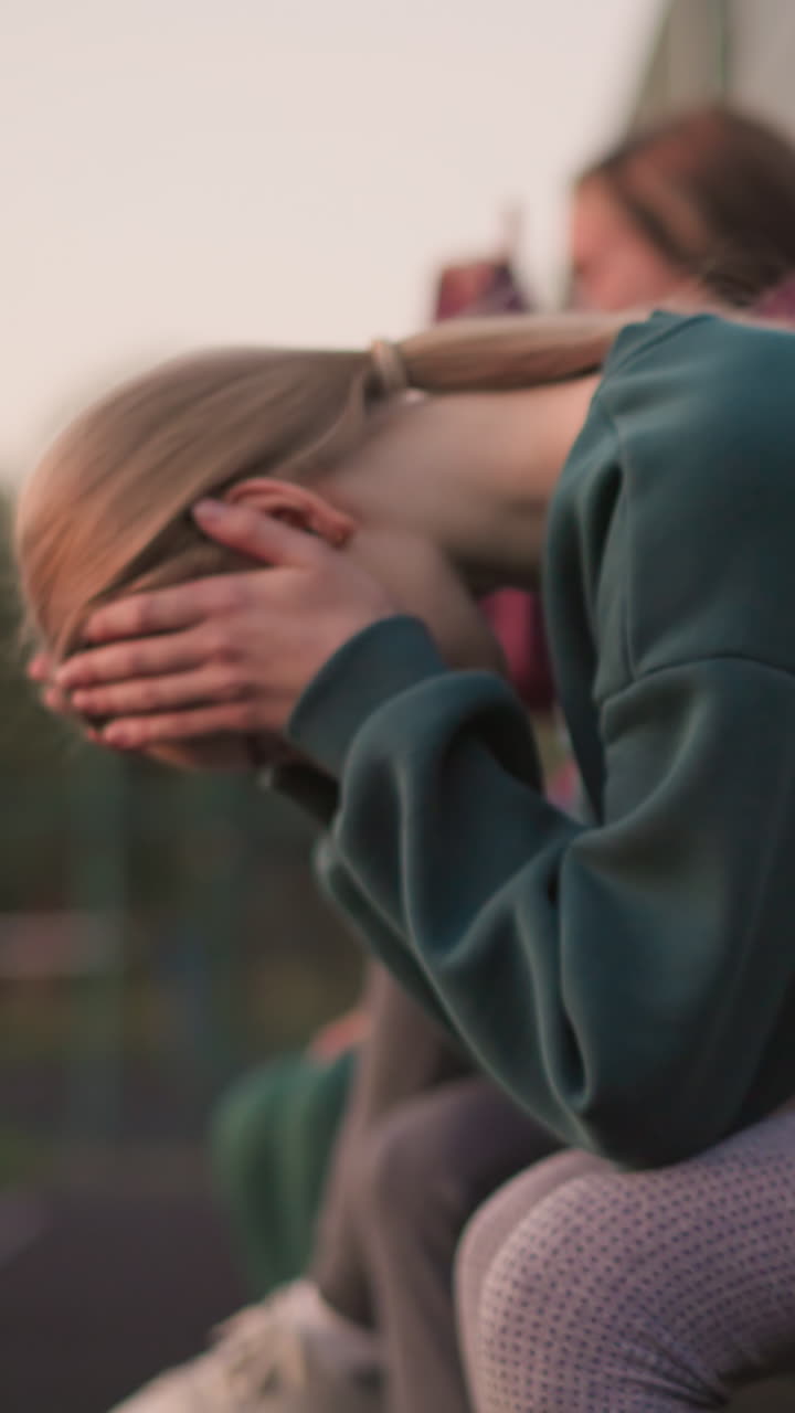 긴 훈련 후 휴식을 취하는 운동선수들의 측면 뷰, 녹색 옷을 입은 한 여인이 휴식을 취하면서 머리를 숙이고, 강렬한 운동 후 회복과 휴식의 순간을 반영합니다.