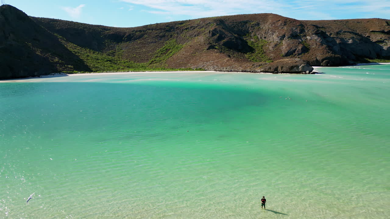 Aerial drone view of crystal clear blue waters with desert mountains in the background along the Baja California coast