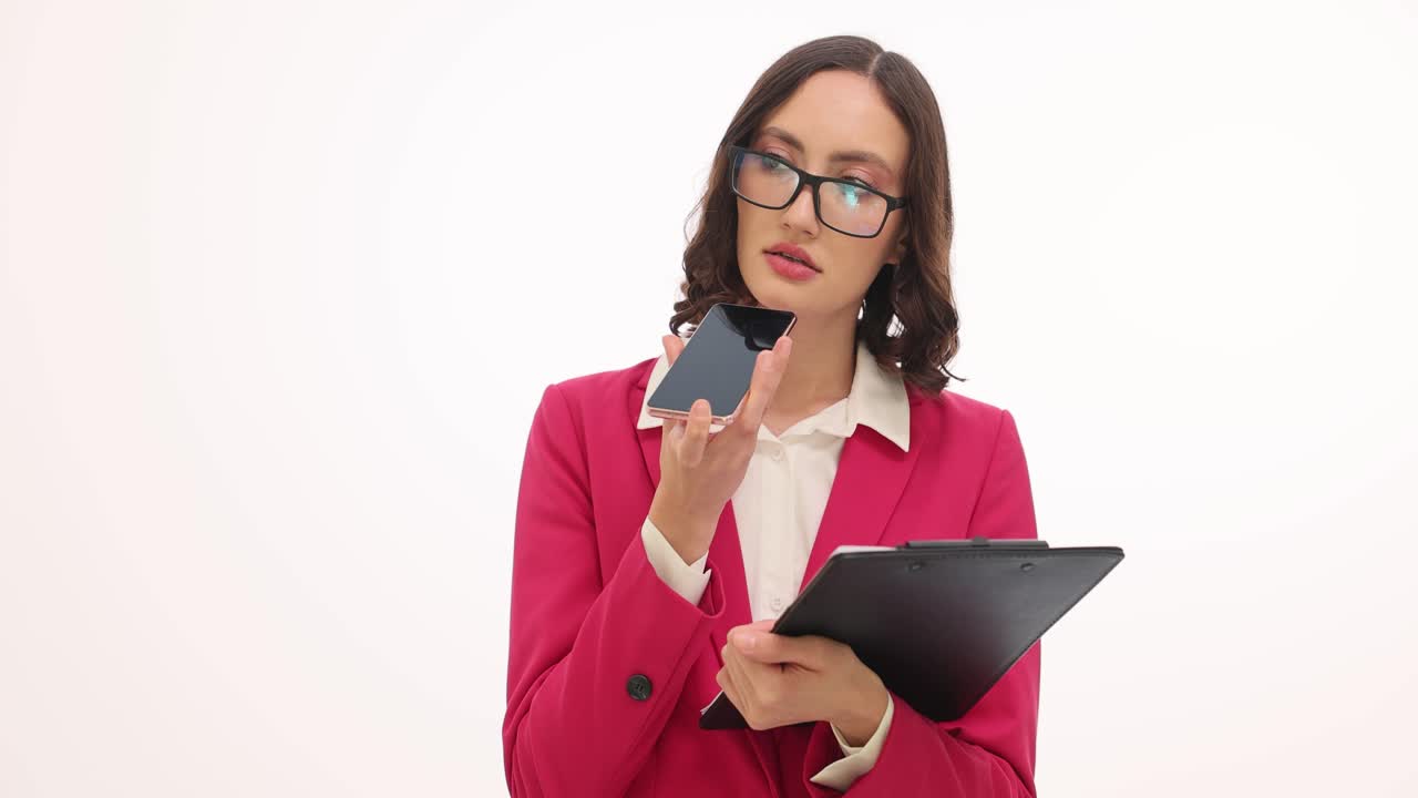 Professional woman in pink blazer and glasses talking on smartphone with clipboard