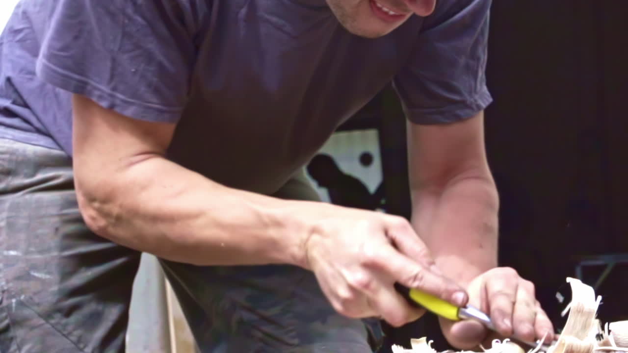 Close-up of a person carving wood with a chisel, generating wood shavings