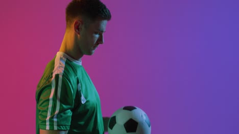 Caucasian-male-soccer-player-with-football-over-neon-pink-lighting