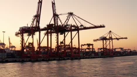sunset at the port: cargo cranes silhouetted against a golden sky, showcasing maritime industry in action with containers lined up along the water's edge