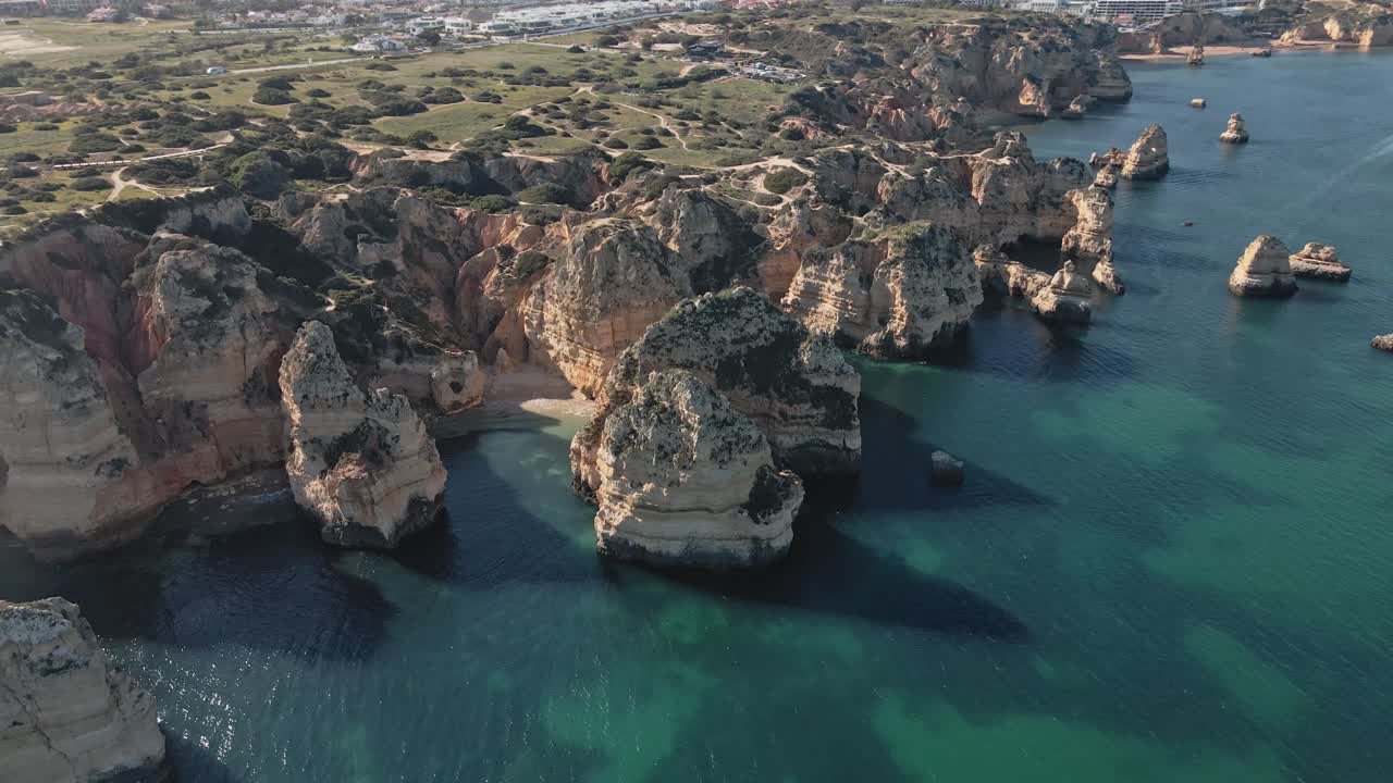 Aerial drone performs a dynamic helix orbit, circling high above the dramatic golden limestone stacks and hidden coves along the coast near Lagos, Portugal