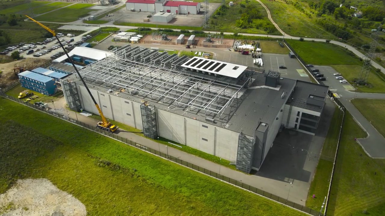 Luftperspektiv af en stor datacenterbygning under opførelse med en gul kran, der aktivt arbejder på taget og installerer stålrammekonstruktioner og kølesystemer til anlægget
