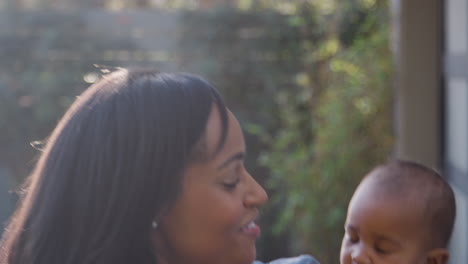 portrait of smiling african american mother cuddling and playing with baby daughter in garden