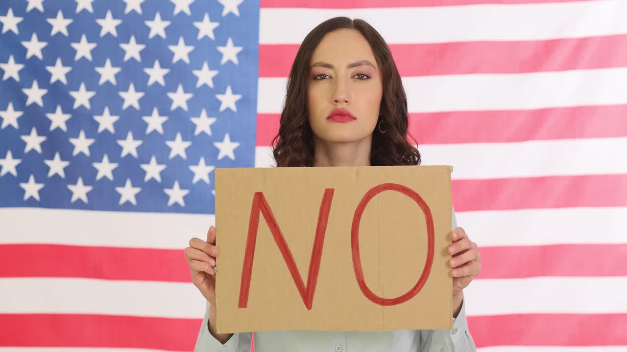 Woman holding a 'NO' sign in front of an American flag