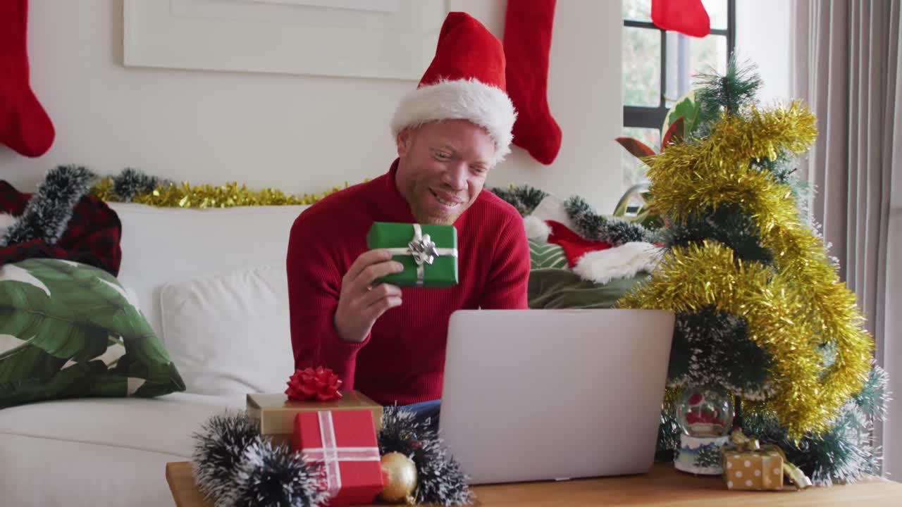 hombre afroamericano albino feliz con sombrero de papá noel haciendo una videollamada en navidad