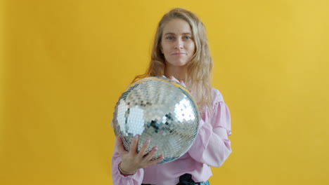 woman holding a disco ball against a yellow background