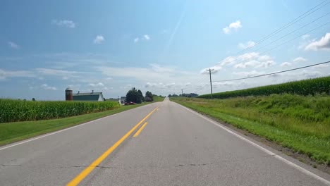 pov - driving on a country road past rural homes, farmyards and bean fields in late summer in central iowa