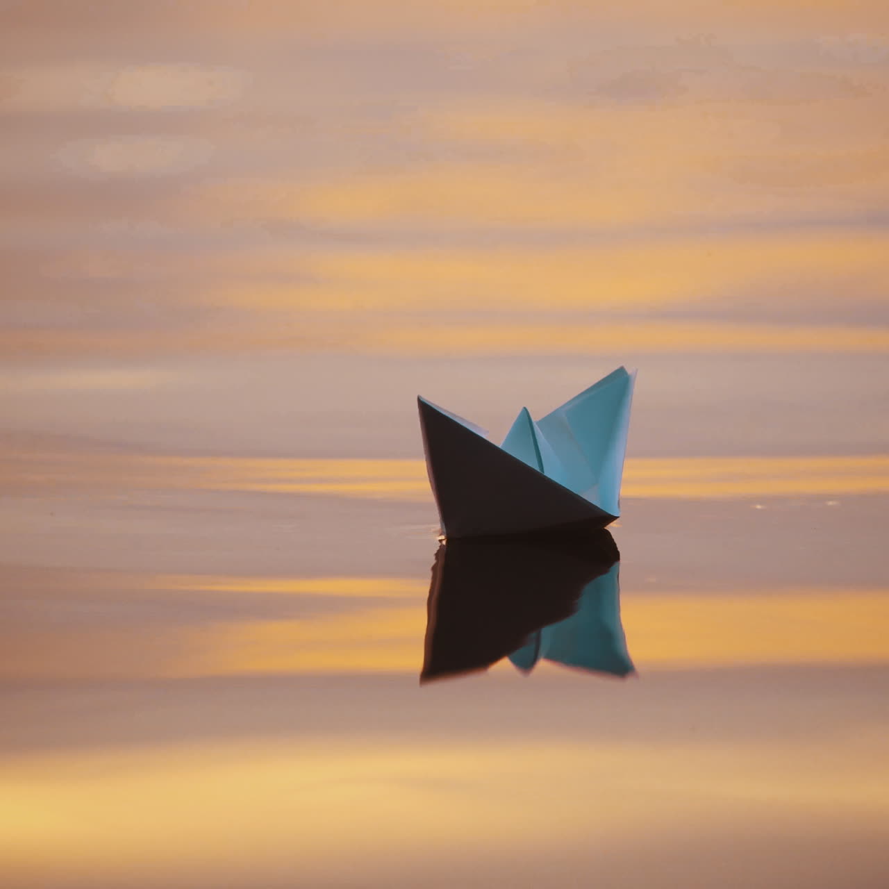 Origami boat on water surface in the evening. White paper boat swims with its shadow reflection in water. Close-up.