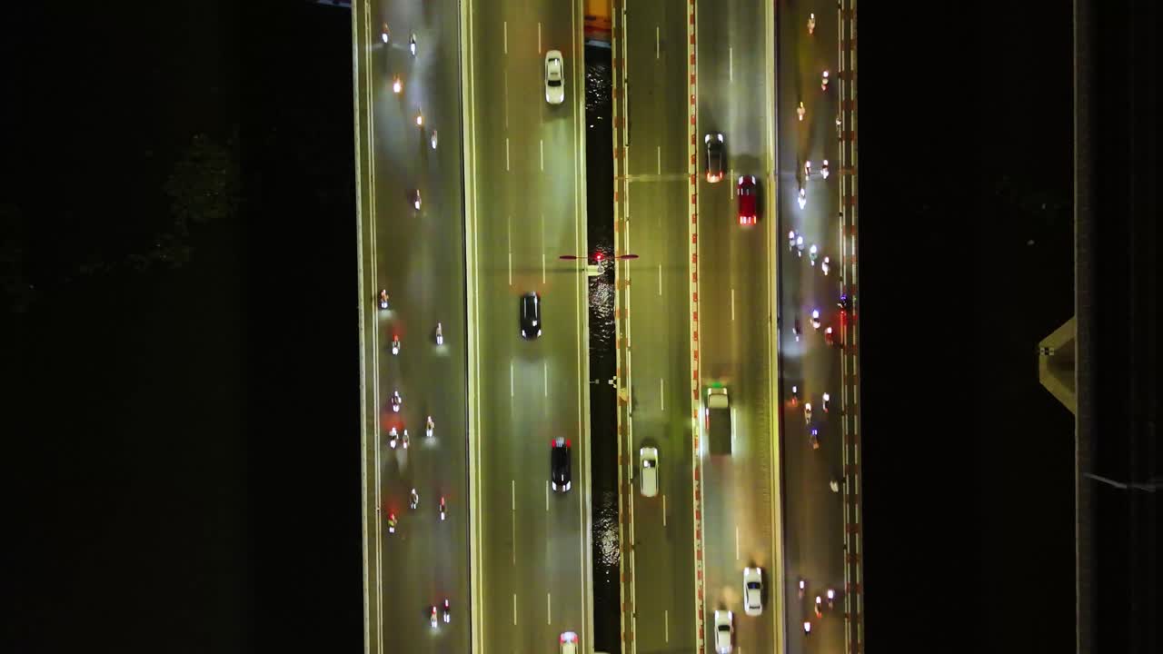 Top-down aerial view of heavy traffic on a central bridge over the Saigon River in Ho Chi Minh City, Vietnam, illuminated by city lights and billboard signs.