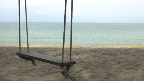 close up one wooden swing on the beach, no people, blurred background of sea and sky