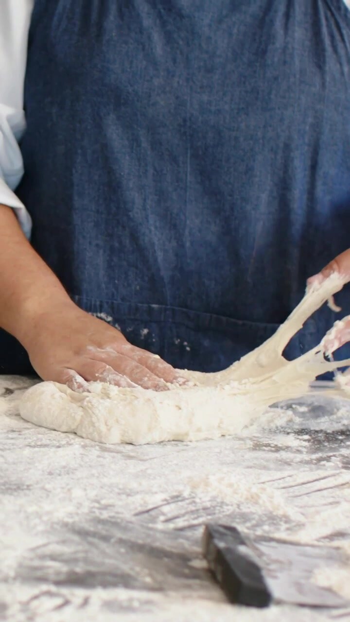 Vertical video: Camera focusing hands in bakery, chef in apron kneading dough for bread, scraper
