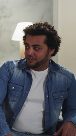 happy black guy tells funny story to bearded friend with kinky hair spending time together in living room. african-american friends communicate in room resting