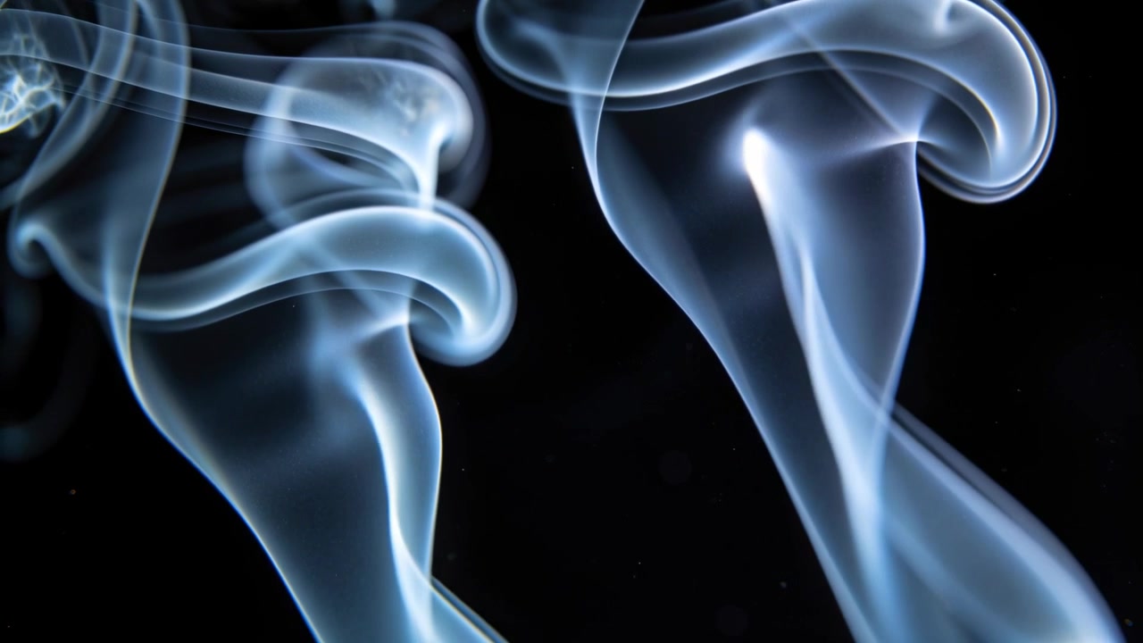 Due alte colonne di fumo che emergono, si alzano e si attorcigliano con volute in uno studio buio, con retroilluminazione.