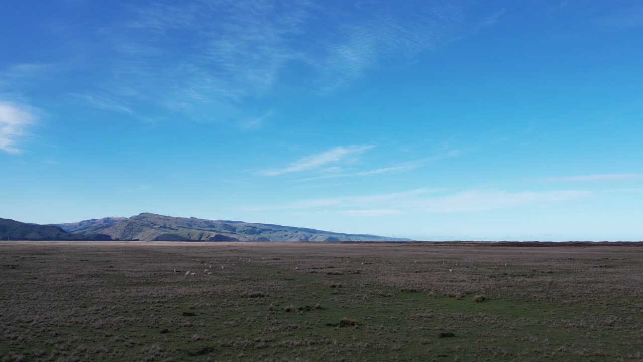 ganando altitud sobre un vasto paisaje con el sol cayendo en colinas distantes y el océano - kaitorete spit, nueva zelanda