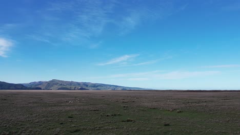 ganando altitud sobre un vasto paisaje con el sol cayendo en colinas distantes y el océano - kaitorete spit, nueva zelanda