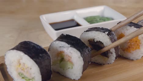 medium slow motion slider shot of taking a piece of sushi from a wooden serving board with chopsticks and dipping into soy sauce