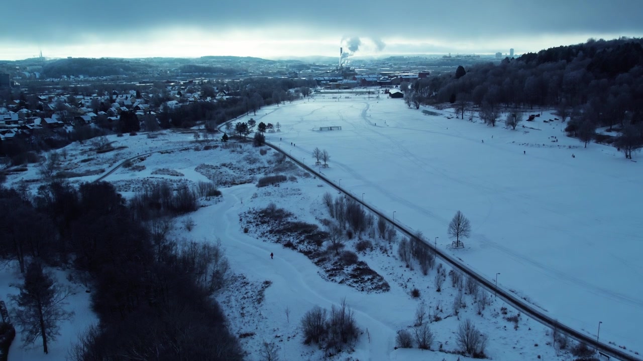 Veduta aerea con drone del Parco Kviberg coperto di neve durante l'inverno a Göteborg, Svezia, con ampi spazi verdi, paesaggio ghiacciato, sentieri tortuosi e lo skyline urbano circostante