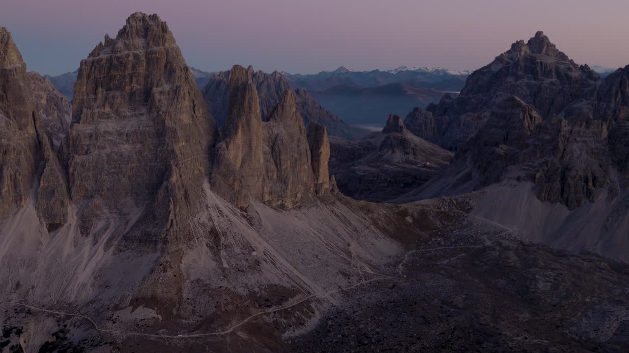 Vista aerea cinematografica delle Dolomiti in Italia, cime alpine frastagliate che si illuminano all'alba, pareti a strapiombo mozzafiato e profonde valli in ombra che creano un'atmosfera serena ad alta quota