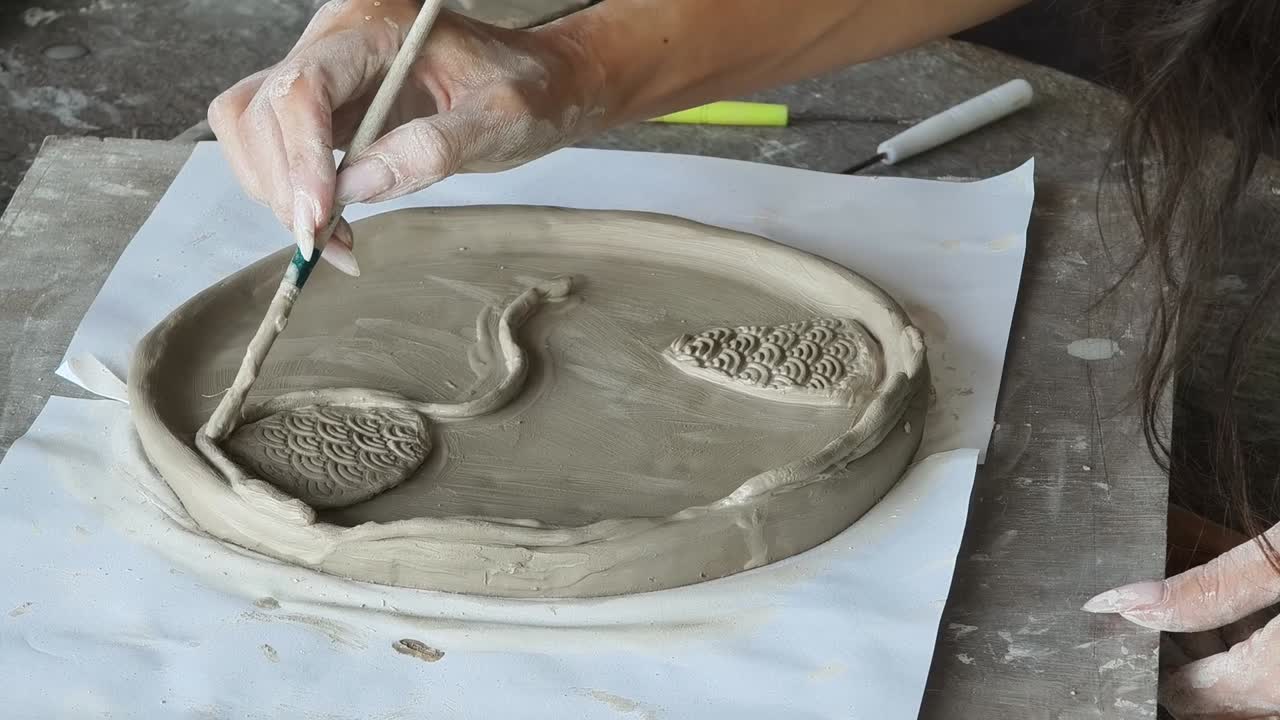 Artista alisando plato de arcilla con un pincel en un taller de cerámica