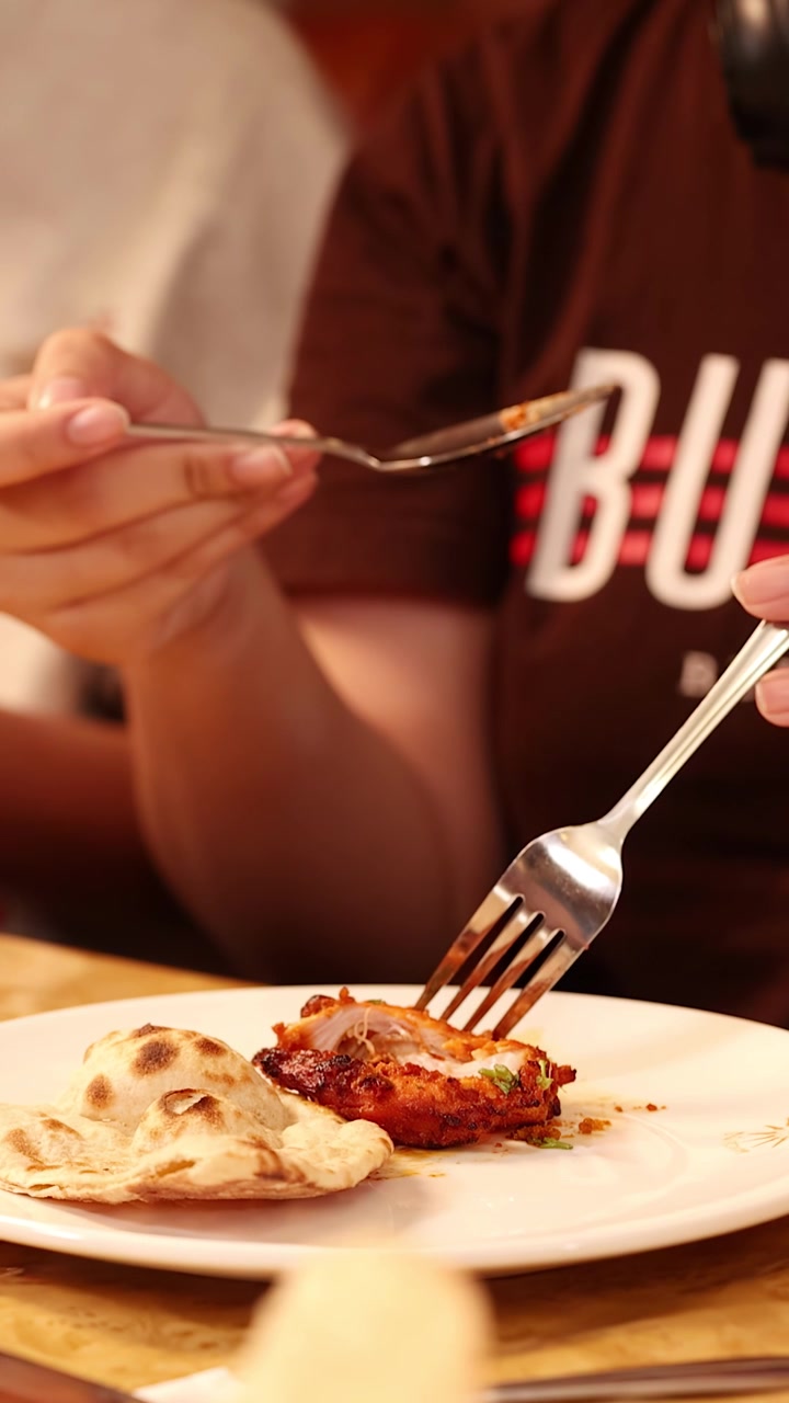Close-up shot of diners using forks and spoons to eat Indian cuisine in a restaurant.