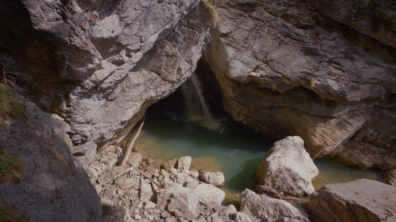 Clear turquoise mountain water in a rock pool, waterfall from a dark cave opening. Starzlachklamm gorge