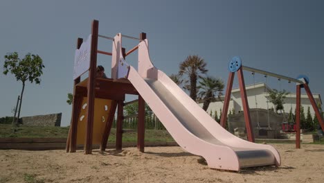 Young-girl-playing-on-a-slide-in-a-playground-on-a-warm-sunny-day