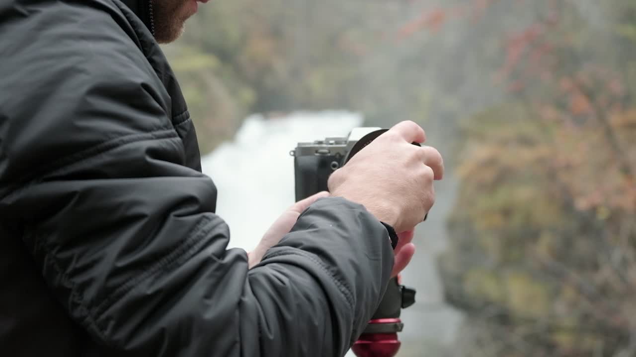 el fotógrafo masculino blanco adjunta el fondo de la cascada de la cámara del parasol